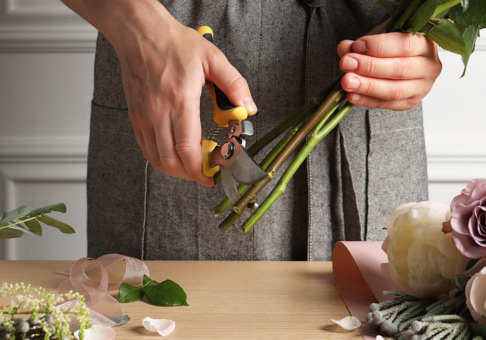 A male pair of hands carefully trims the stems of a flower grouping