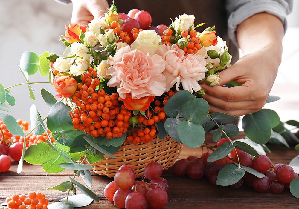 A local floral designer heaps pink, orange and red flowers and berries into a large gift basket